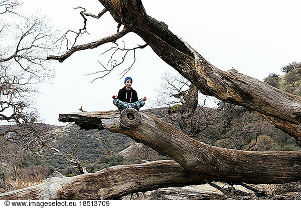 Teen boy meditates atop of a fallen tree