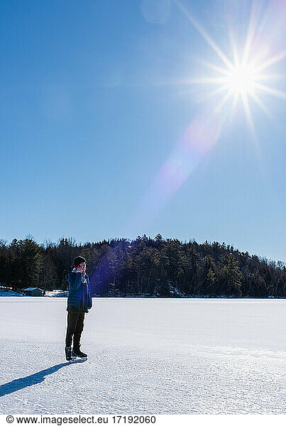 Teen boy on smart phone and skates on a frozen lake on a winter's day.