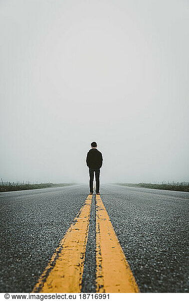 Teen boy standing in middle of rural road on a foggy day.