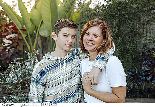 Teen boy with arm around smiling mom's shoulder outdoors