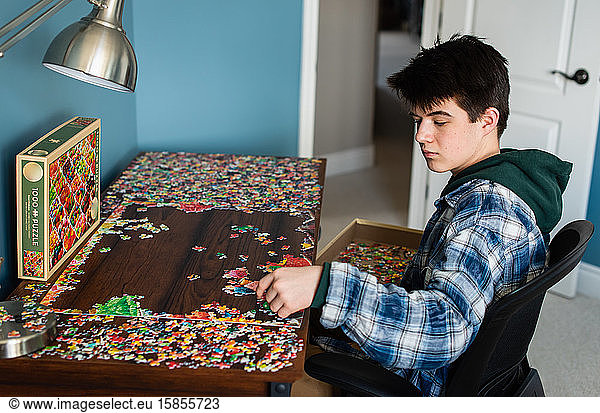 Teen boy working on a jigsaw puzzle in his bedroom during Covid 19.
