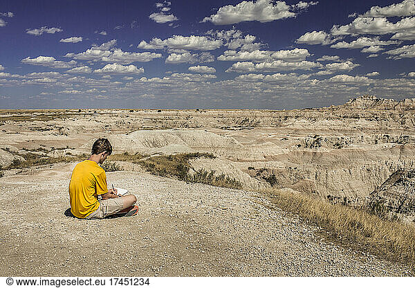 Teen boy writes in notebook overlooking Badlands National Park  USA