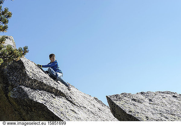 Teen climbing on rock while looking away in a sunny day