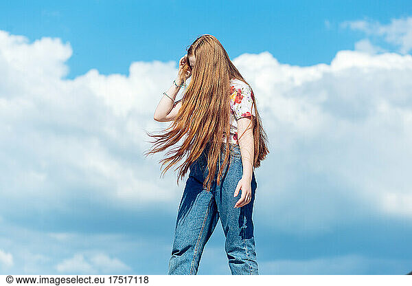 Teen ginger girl with long hair standing on the blue cloudy sky
