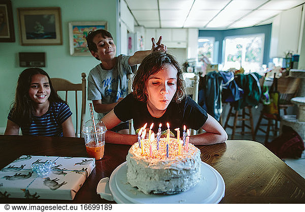 Teen girl blows out candles of her birthday cake with siblings near