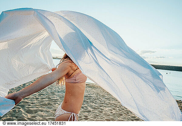 Teen girl flipping sheet over head at the lake on a summer day