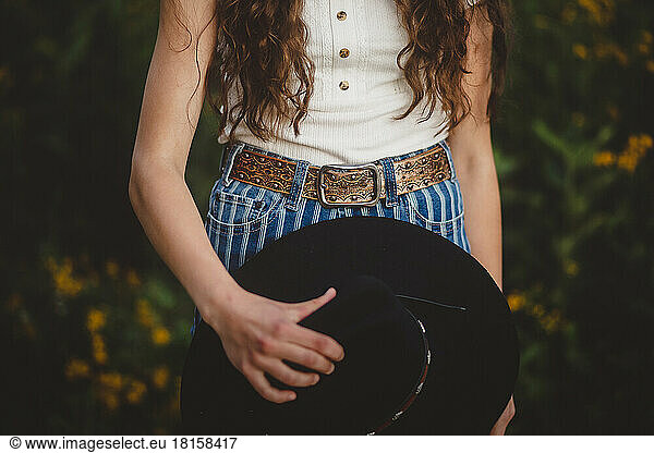 teen girl holding cowboy hat by belt buckle