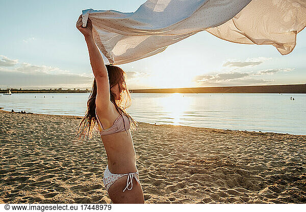 Teen girl playing with white sheet at sunset on the beach