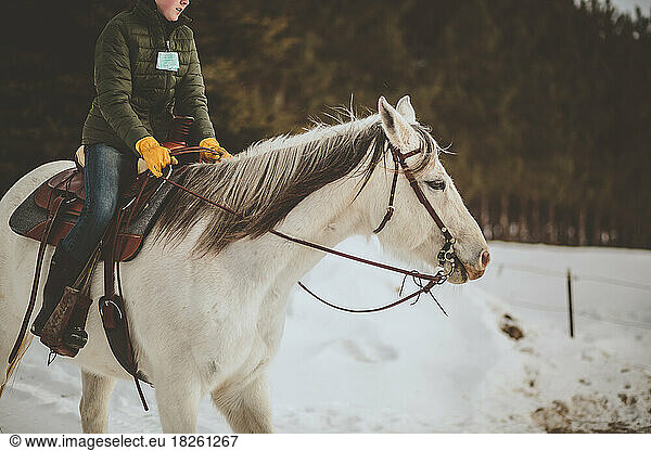 Teen girl riding white horse in winter