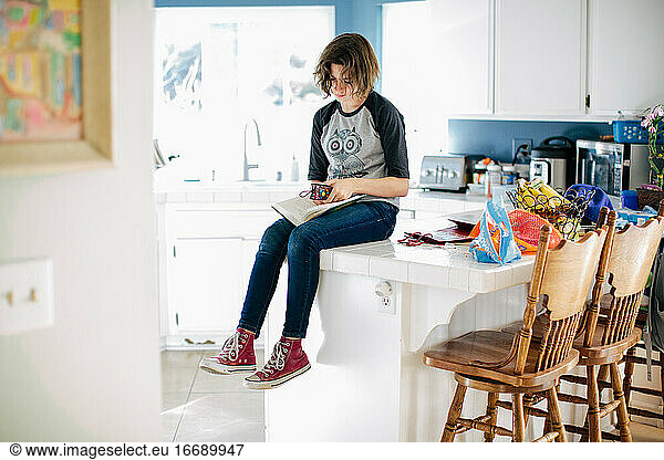 Teen girl sits on kitchen counter and places her bookmark in her book