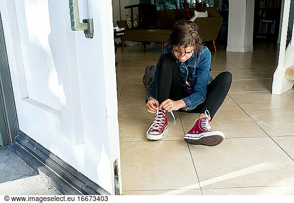 Teen girl sits on the tile floor and ties her brand new shoes