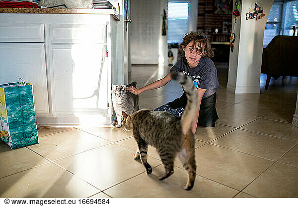 Teen girl sits on the tile floor petting one of two cats