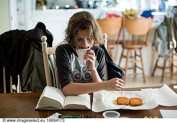 Teen girl takes a bite of a hash brown while she reads her book