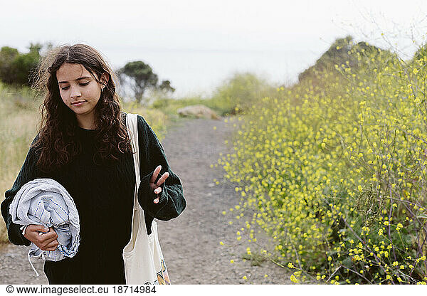 Teen Girl Walking Away From Beach On A Trail Next To Wildflowers