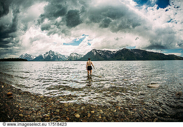 Teen girl walking in alpine lake with snowy mountains in background