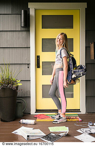 Teen Girl Wearing Backpack Stands by Yellow Door with Books on Ground