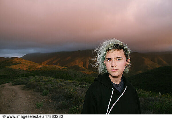 Teen Girl With Blue Hair Under Pink Clouds On Top Of a Mountain