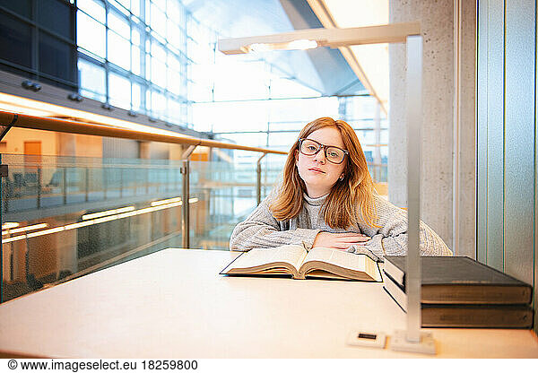 Teen girl with red hair and glasses reading at the library.