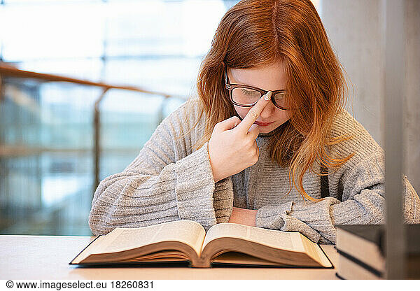 Teen girl with red hair studying at urban library.