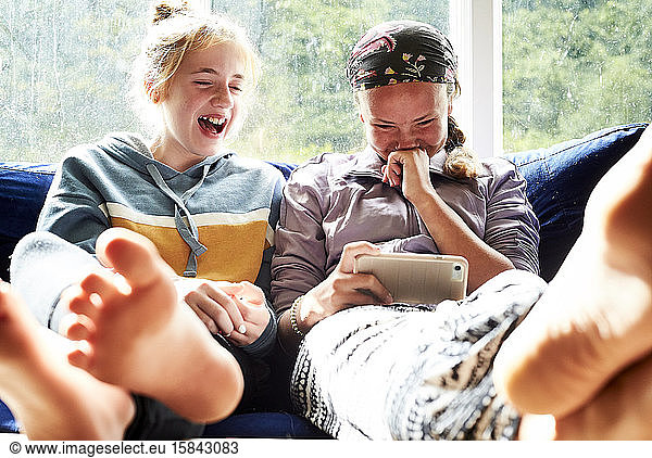Teen girls laughing on a couch looking at something on a phone