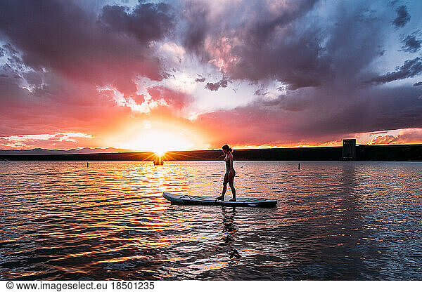 Teen paddle boarding at sunset