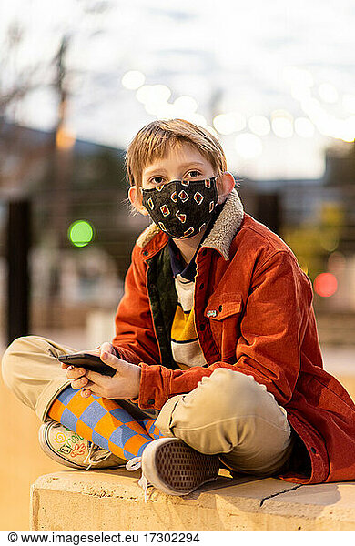Teen sitting holding phone wearing mask during Global Pandemic