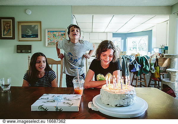 Teen stares at the candles on her cake while siblings sing
