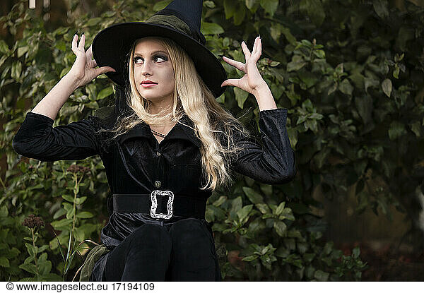 Teen/Tween Girl Dressed in Black Witch Halloween Costume Near Greenery