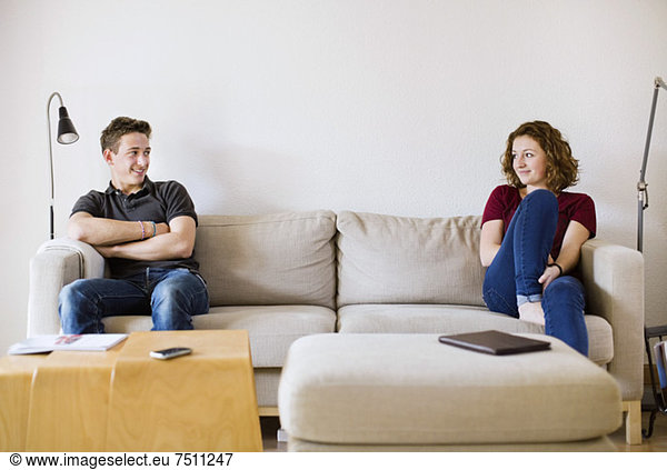 Teenage boy and girl looking at each other while sitting on sofa