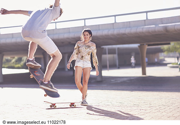Teenage boy and girl skateboarding at sunny skate park