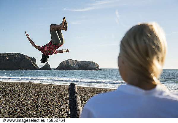 Teenage boy back flipping off see-saw on beach