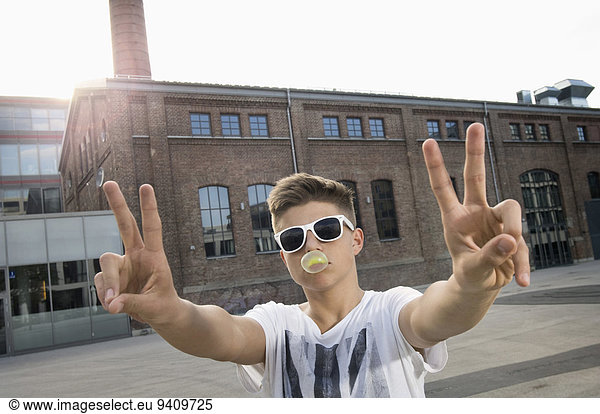 Teenage boy blowing bubble gum and showing peace sign
