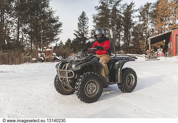 Teenage boy driving quadbike on snowy field