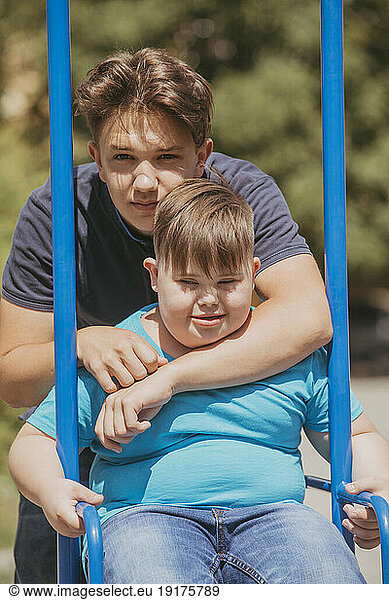 Teenage boy embracing brother with down syndrome sitting on swing
