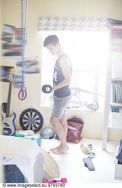 Teenage boy exercising with dumb bell in his room