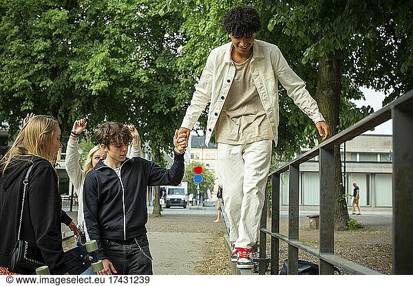 Teenage boy holding hand of male friend walking on railing
