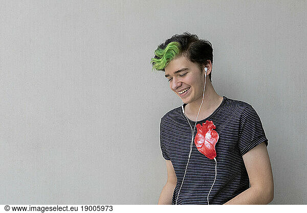 Teenage boy listening to heartbeat with headphones against gray background
