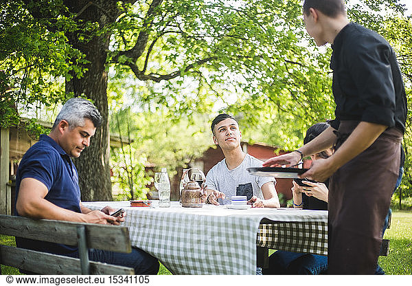 Teenage boy looking at waiter while sitting with friends in restaurant