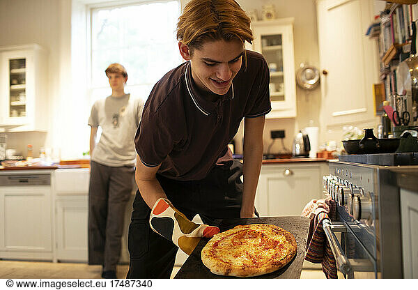 Teenage boy making pizza in kitchen