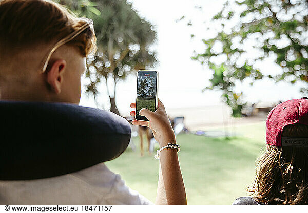 Teenage boy photographing through smart phone by sister during vacation