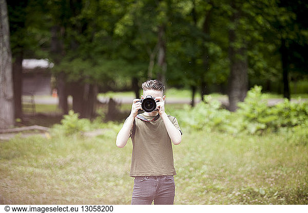 Teenage boy photographing while standing on field