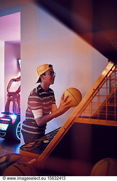 Teenage boy playing basketball in an amusement arcade