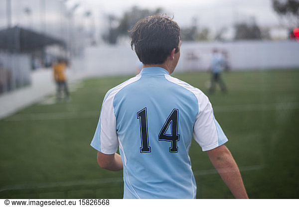 Teenage boy playing indoor soccer wearing light blue jersey number 14