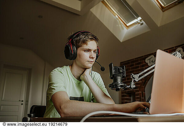 Teenage boy podcasting in front of laptop at home