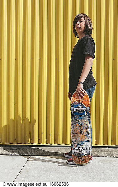 Teenage boy posing with skateboard in front of urban warehouse