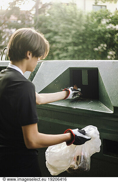 Teenage boy putting plastic garbage in recycling bin