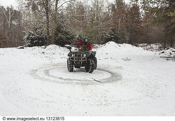 Teenage boy riding quadbike on snowy field