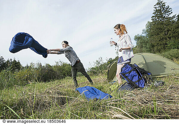 Teenage boy shaking sleeping bag in front of camp tent in forest  Bavaria  Germany