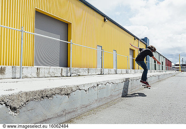 Teenage boy skateboarding in front of industrial warehouse loading zone