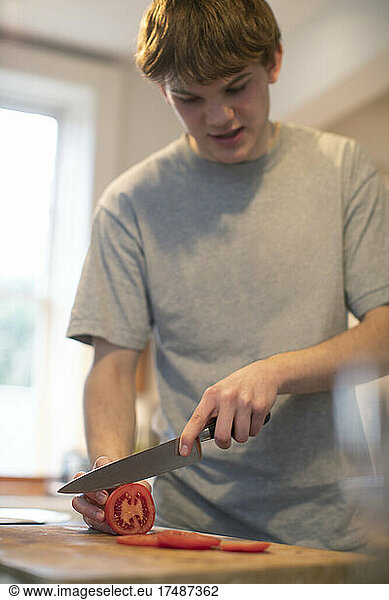 Teenage boy slicing fresh tomato in kitchen
